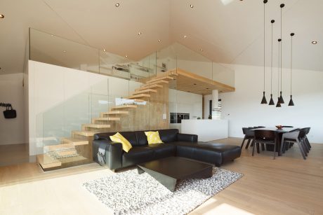 A modern, open-concept living space with a glass staircase, sleek furniture, and pendant lighting.