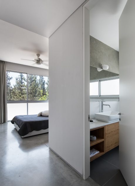 Minimalist bedroom with modern en-suite bathroom and large window overlooking greenery.