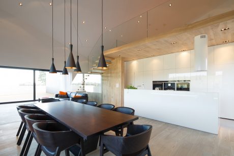 Modern open-concept kitchen and dining area with wooden beams, pendant lights, and sleek furnishings.