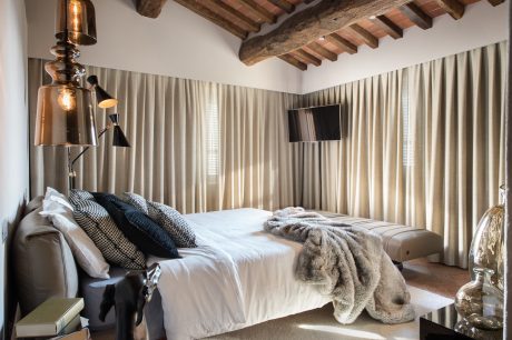 Cozy rustic bedroom with exposed wooden beams and curtain-framed windows creating a warm atmosphere.