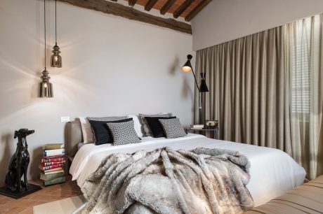 Cozy bedroom with exposed wooden ceiling beams, pendant lighting, and plush bedding.