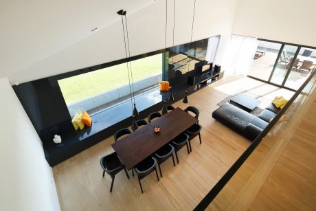 Sleek, modern open-plan interior with large windows, dark furniture, and wooden flooring.