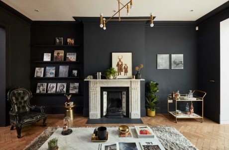 A moody, eclectic living room with black walls, ornate fireplace, and mid-century furnishings.
