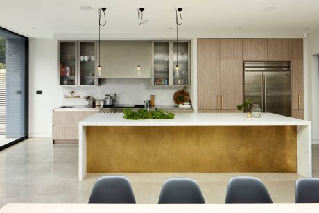 Sleek modern kitchen with wood cabinets, white countertops, and a striking gold-toned island.