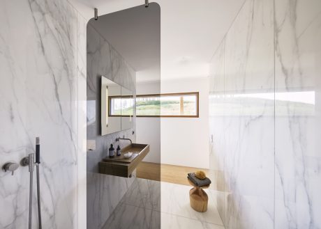 Modern minimalist bathroom with marble walls, wood vanity, and panoramic window.