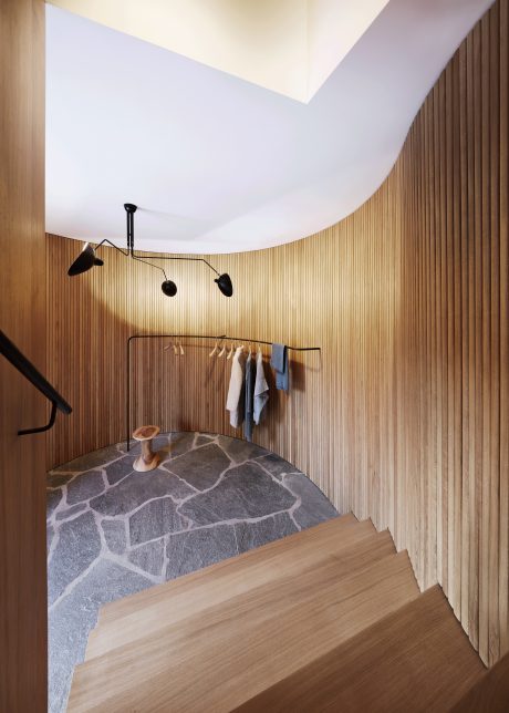A modern, minimalist hallway with wooden paneling, a stone-tiled floor, and a hanging clothing rack.