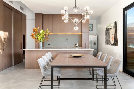 Modern kitchen and dining area with wooden cabinetry, sleek light fixtures, and minimalist furniture.