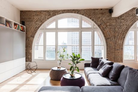 A bright, contemporary living room with arched windows, exposed brick walls, and sleek furniture.