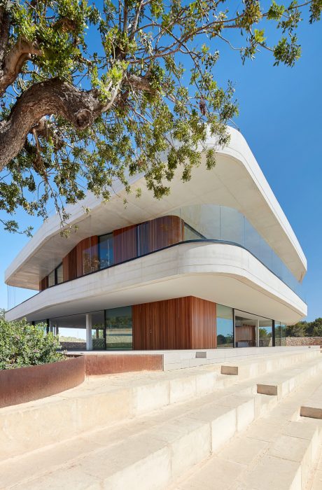 Modern architectural design with curved, concrete exterior, wooden accents, and glass walls.