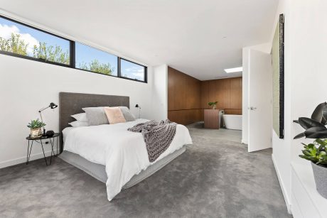 Spacious modern bedroom with high windows, neutral color palette, and en-suite bathroom.