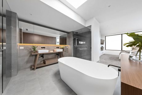 A modern, minimalist bathroom with a freestanding tub, dual vanity, and glass shower enclosure.