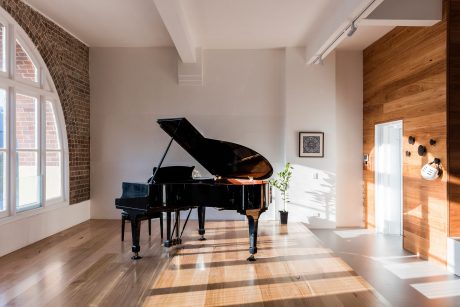 Elegant, wood-paneled room with grand piano and brick accent wall, spotlighting architectural details.