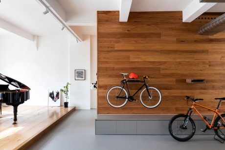 Minimalist loft-style space with wood-paneled walls, bikes displayed, and a grand piano.