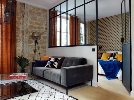 A modern loft with stone walls, steel-framed windows, and a plush gray sofa.