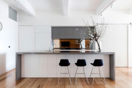 Sleek, modern kitchen with minimalist gray cabinetry, wood accents, and three black bar stools.