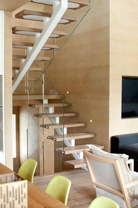 A modern, open-concept staircase with glass railings and wood steps in a bright, airy room.
