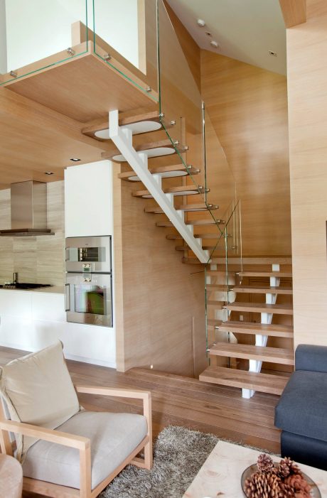 Elegant wooden staircase with glass panels, open-concept living space, and contemporary furnishings.