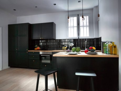 Modern kitchen with black cabinetry, wooden countertop, and pendant lighting.