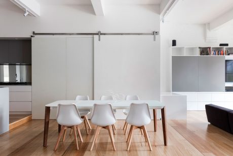 Open-concept modern apartment with minimalist dining table, chairs, and built-in shelving.