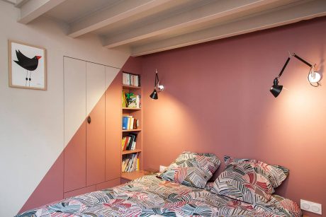 A cozy bedroom with a wooden ceiling, built-in shelves, and a vibrant pink accent wall.