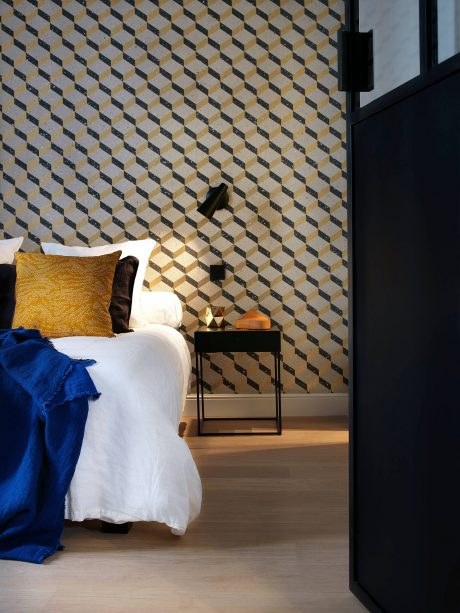 Geometric patterned wall, minimalist nightstand, and blue bedding create a cozy yet chic bedroom.