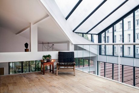 A modern, minimalist indoor space with floor-to-ceiling windows, glass railings, and wooden floors.