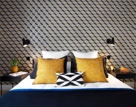 Geometric wallpaper, black bedposts, yellow patterned pillows, and a monochrome accent pillow.