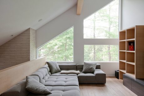 Spacious living room with large windows overlooking natural scenery, minimalist shelving, and a cozy gray sectional sofa.