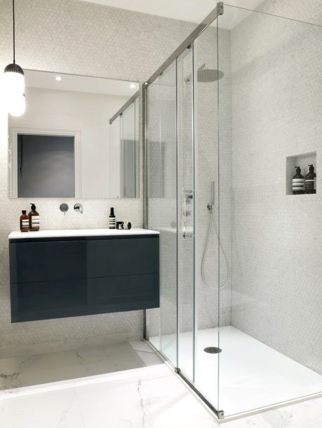 Modern bathroom with sleek black vanity, glass shower enclosure, and marble-like tile flooring.