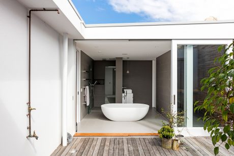 Spacious, well-lit bathroom with modern freestanding tub and glass walls overlooking nature.