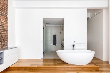 A modern bathroom with a freestanding white bathtub, wooden floor, and a glass-enclosed shower area.