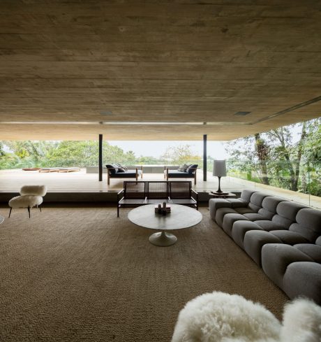 Cozy mid-century modern living room with exposed wood ceiling, wraparound sofa, and views of nature.