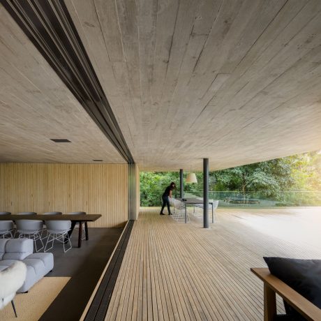 Minimalist interior with concrete ceiling, wooden deck, and glass walls overlooking nature.