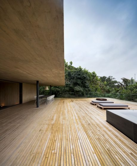 Expansive wooden deck surrounded by lush foliage, minimalist outdoor furniture.