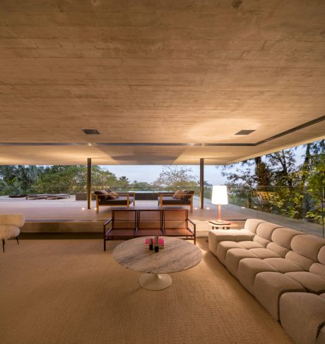 Spacious open-plan living area with wooden ceiling, comfortable seating, and glass walls offering scenic views.