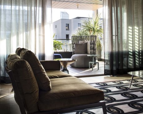 Cozy living room with large sofa, potted plant, and balcony overlooking modern architecture.