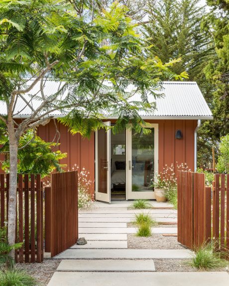 A cozy, rustic cabin nestled in lush greenery, with an inviting entryway and wooden fencing.
