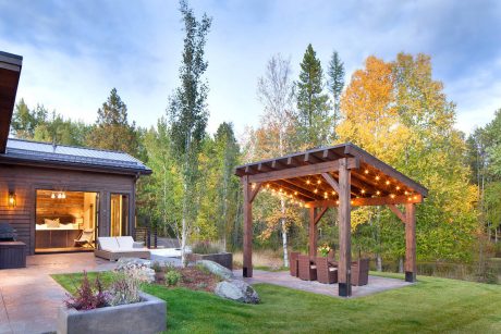 A rustic cabin with a covered patio, surrounded by vibrant autumn foliage and a well-manicured lawn.