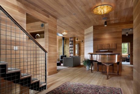 A cozy, warmly-lit interior with wood paneled walls, a fireplace, and a grand piano.