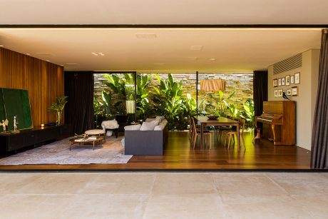 A modern, open-plan living space with lush tropical plants, large windows, and wooden accents.
