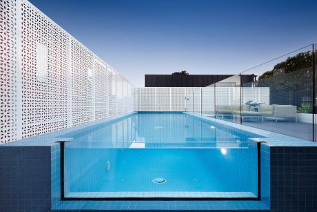 Sleek modern pool area with perforated walls, glass enclosure, and tiled decking.