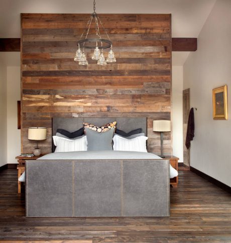 Rustic bedroom with wooden accent wall, modern chandelier, and plush upholstered bed.