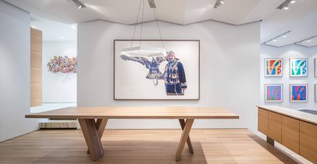 Large wooden table in a modern, minimalist gallery space with colorful artwork on the walls.
