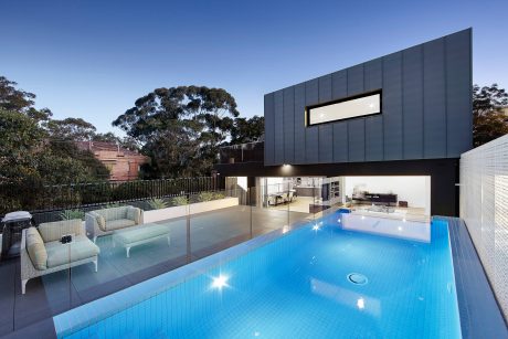Modern home with sleek black exterior, glass walls, and inviting pool area.