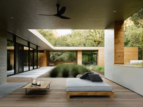Sleek, modern outdoor living space with floor-to-ceiling glass, wooden accents, and lush greenery.
