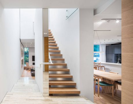 Minimalist staircase design with floating wooden treads and glass railings leads to open living area.