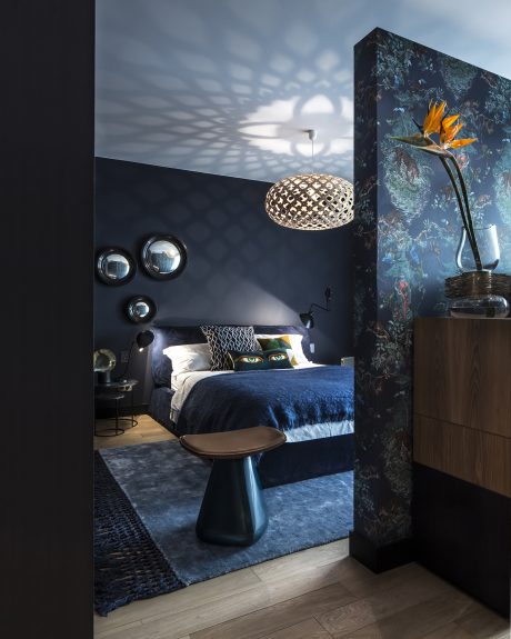 A moody, dark bedroom with eclectic lighting and striking floral wall decor.