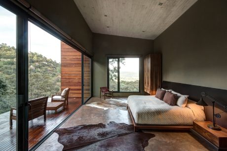 Cozy modern cabin bedroom with panoramic forest view, wood accents, and plush furnishings.