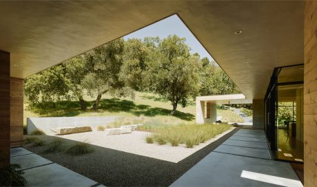 Expansive indoor-outdoor space highlighted by large triangular window revealing lush landscape.