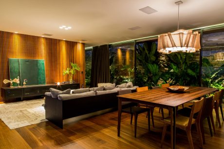 Warm-toned, modern living space with wood furnishings, lush greenery, and dramatic lighting.